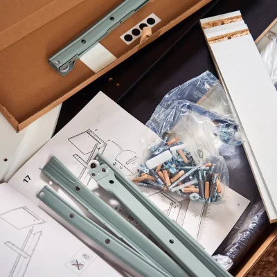 Nahaufnahme eines Möbel-Bausatzes mit Schrauben, Anleitung und Einzelteilen → inhaltsergänzend