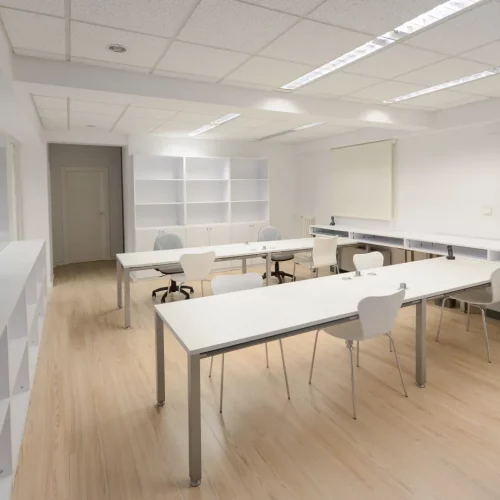 Weißes, minimalistisches Büro mit aufgebauten Tischen, Stühlen und Regalen
